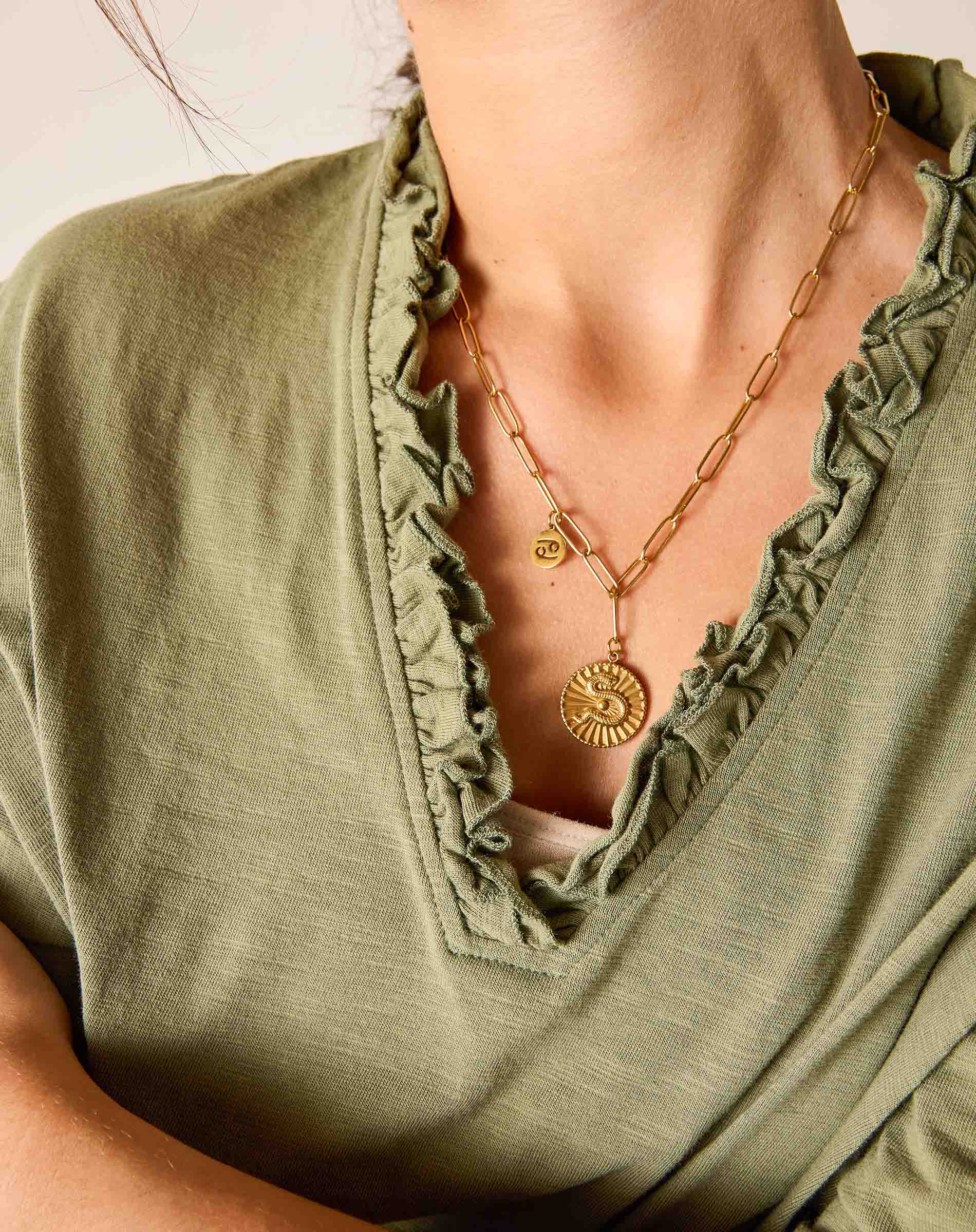 Gold necklace with a pendant on a person wearing an olive green top.