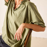 Person wearing a green blouse with ruffled details on a plain background
