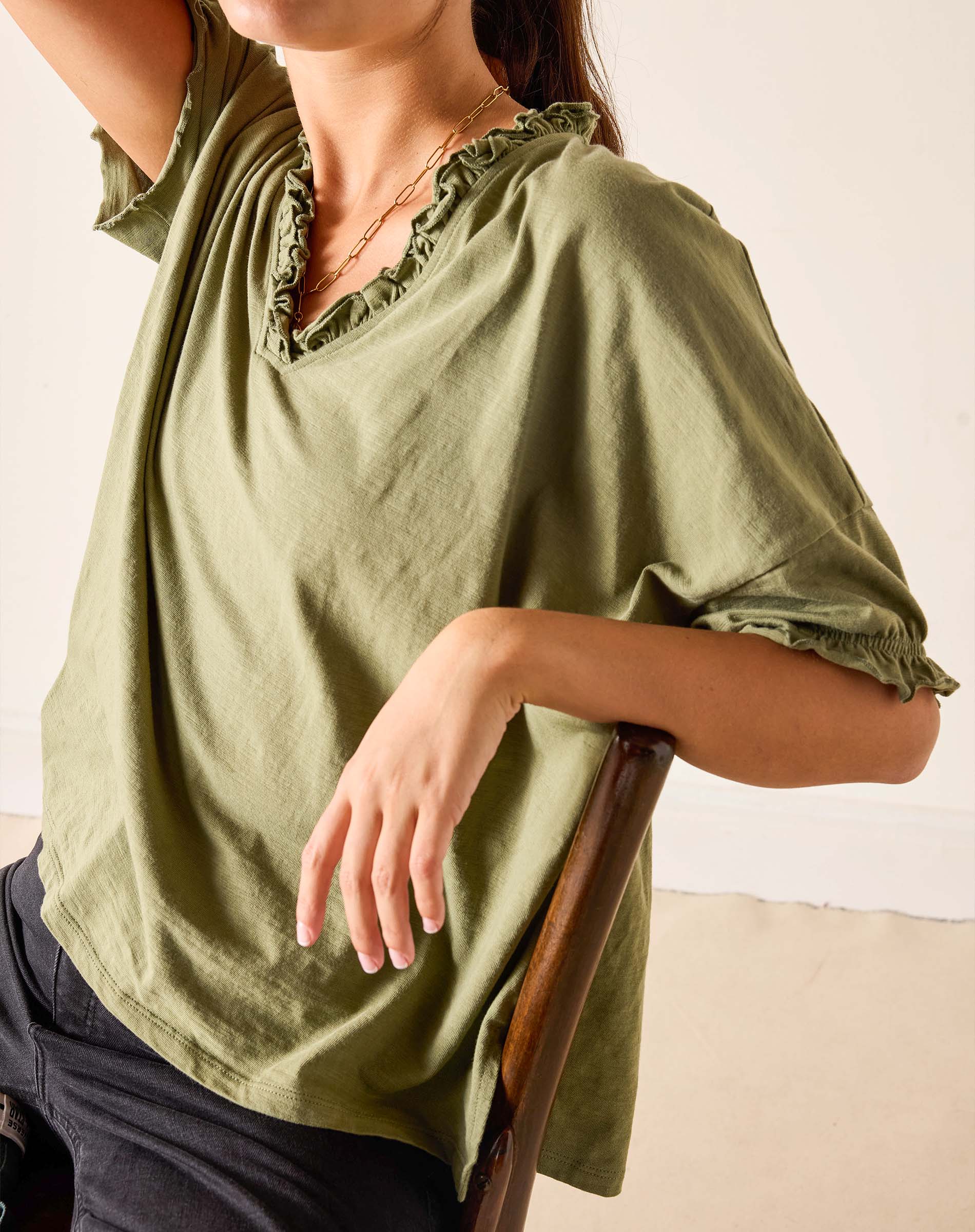 Person wearing a green blouse with ruffled details on a plain background