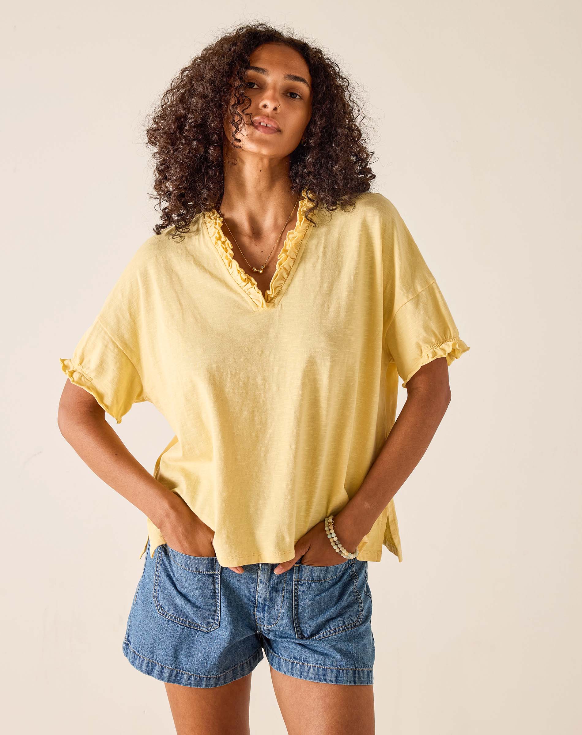 Woman wearing a yellow top and denim shorts against a beige background