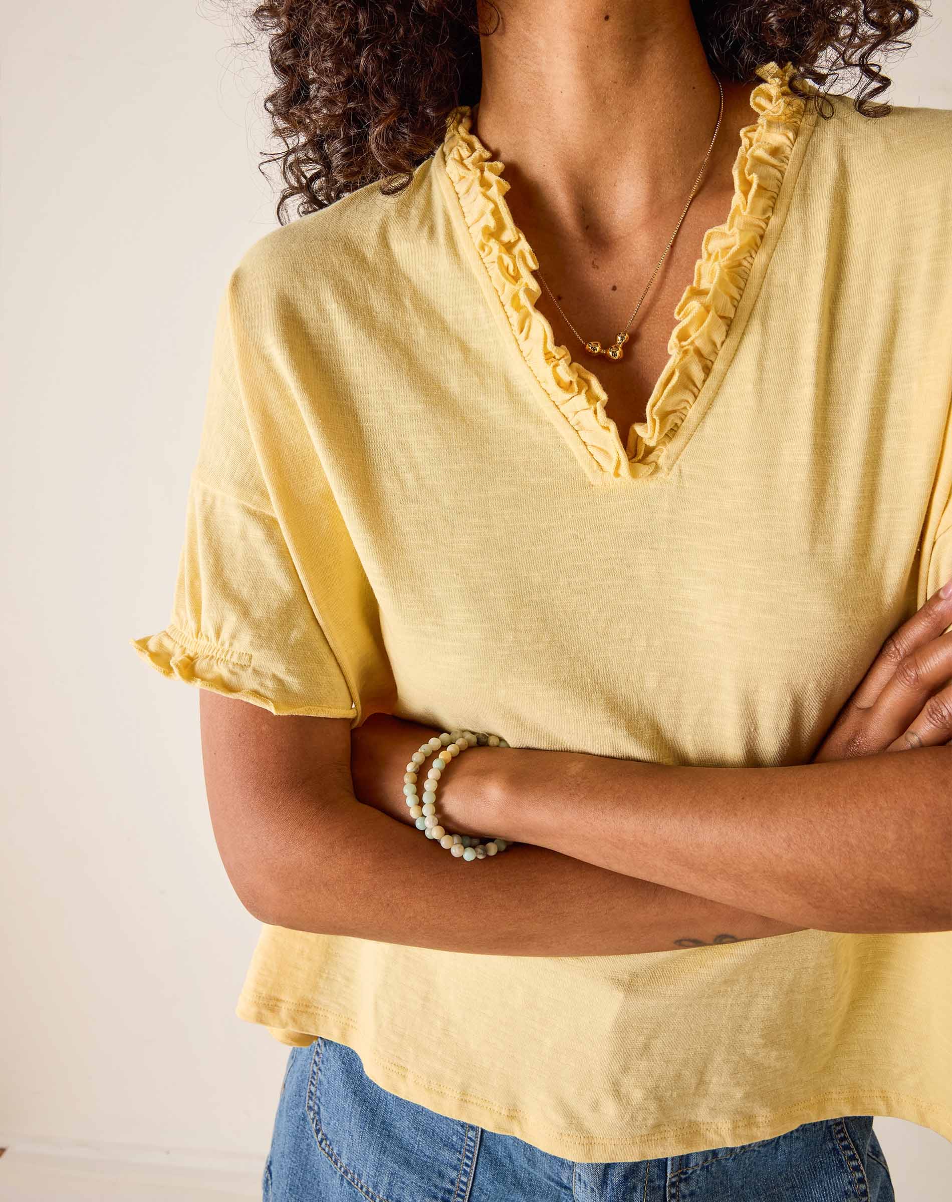 Person wearing a yellow blouse with ruffled neckline and blue jeans against a plain background