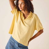 Woman wearing a yellow top and blue shorts against a plain background