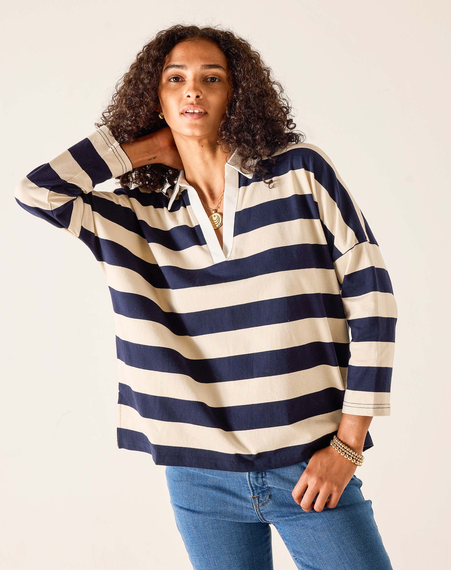 Woman wearing a navy and white striped shirt with blue jeans on a plain background