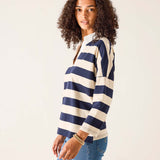 Woman wearing a navy and white striped sweater with blue jeans on a plain background