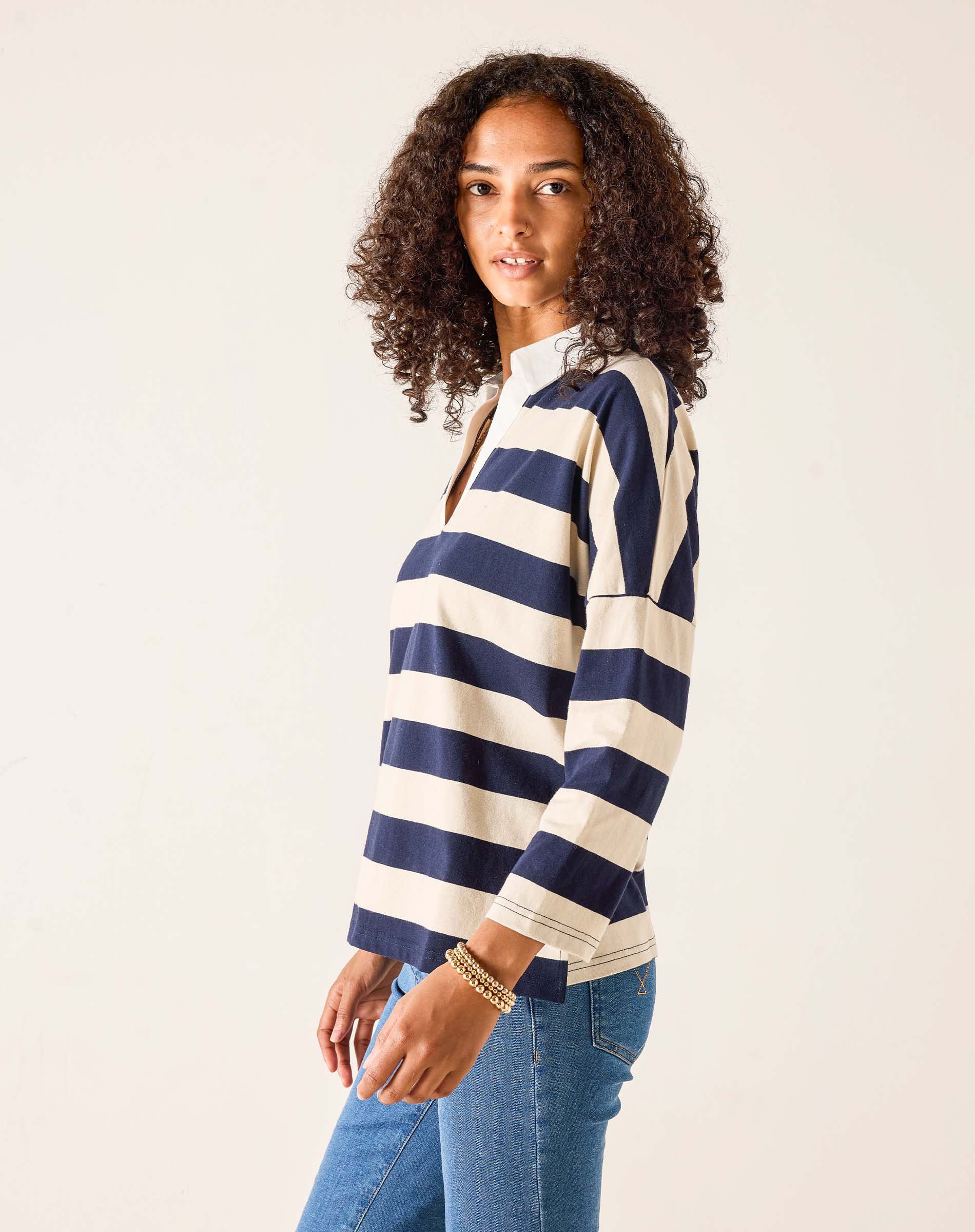 Woman wearing a navy and white striped sweater with blue jeans on a plain background