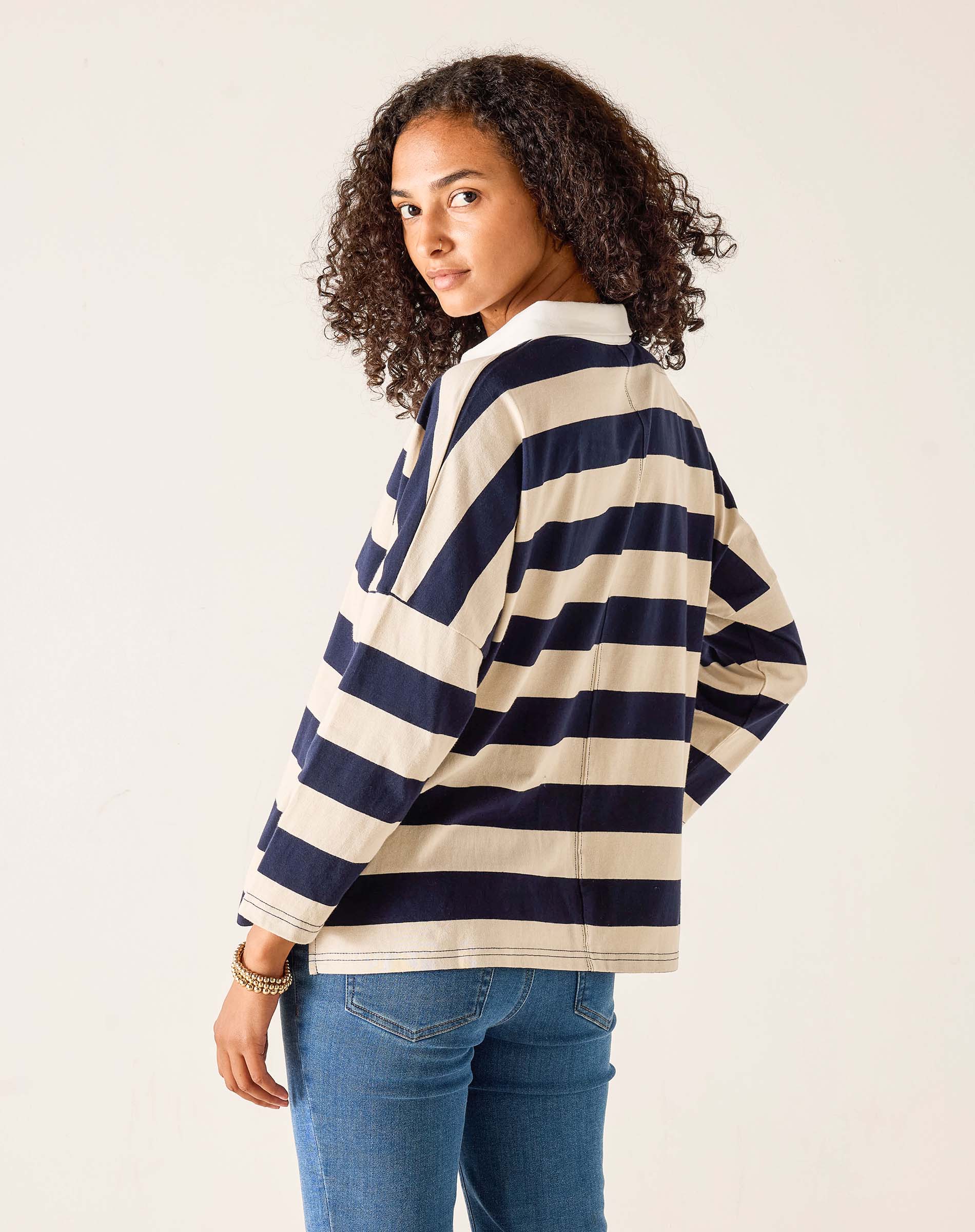Woman wearing a navy and white striped sweater with blue jeans on a plain background