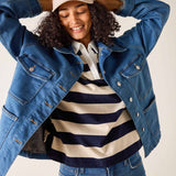 Person wearing a blue denim jacket, striped shirt, and cap on a plain background
