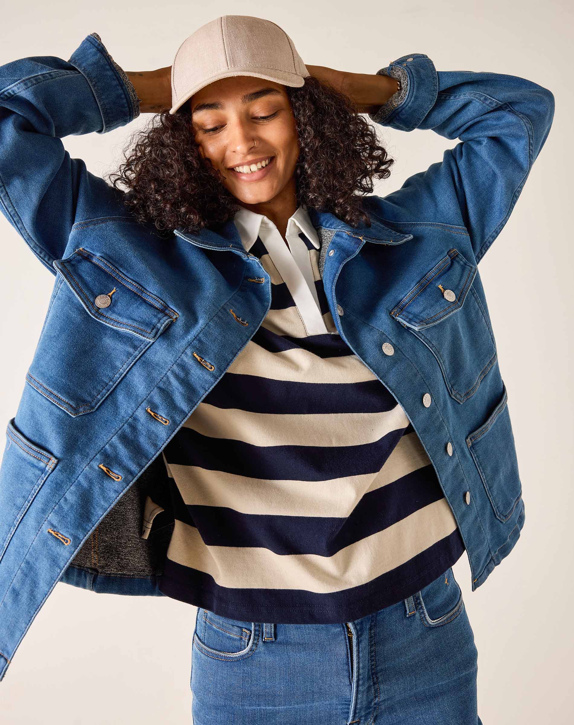 Person wearing a blue denim jacket, striped shirt, and cap on a plain background