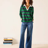 Woman wearing a green and navy striped sweater with blue jeans against a white background