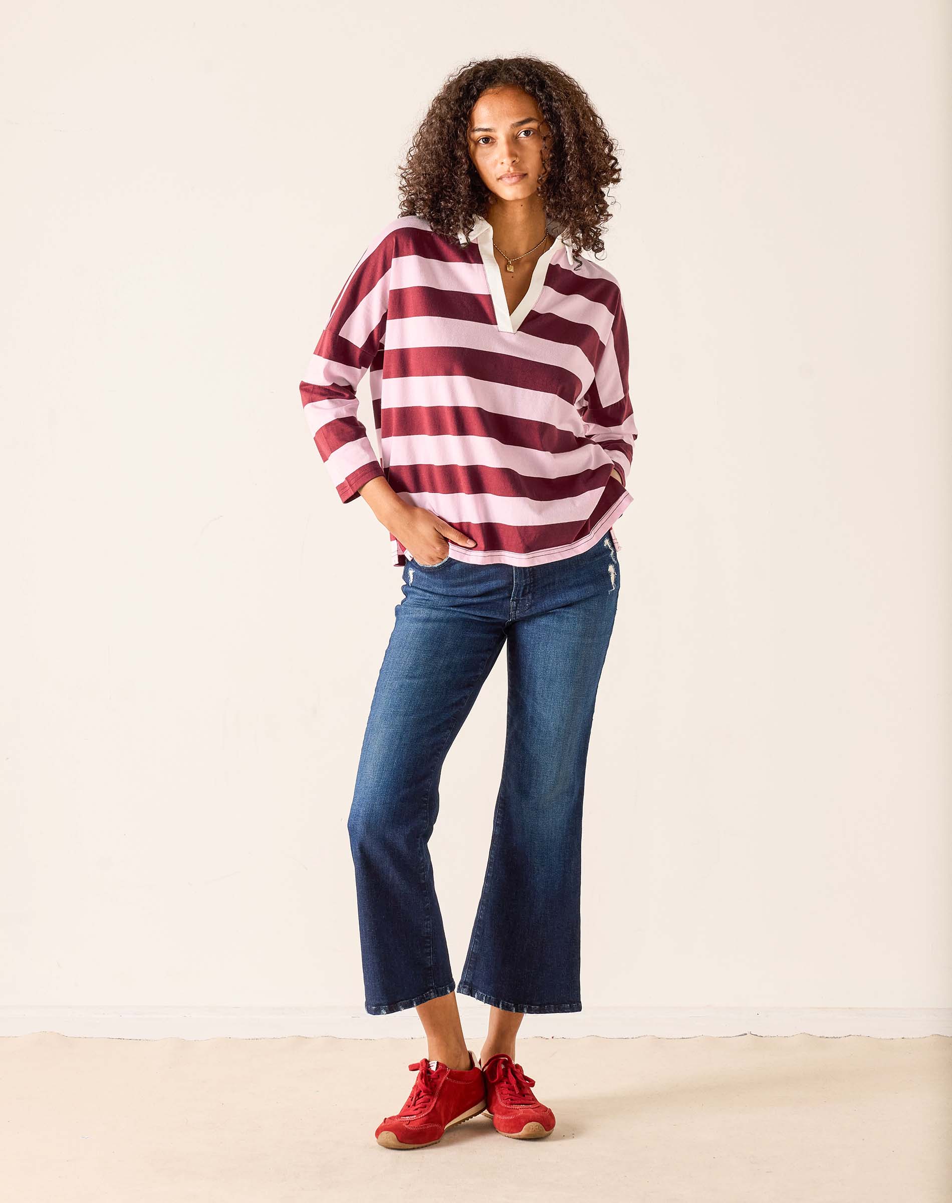 Woman wearing a red and white striped shirt with blue jeans on a plain background