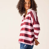 Woman wearing a maroon and white striped shirt with blue jeans on a beige background