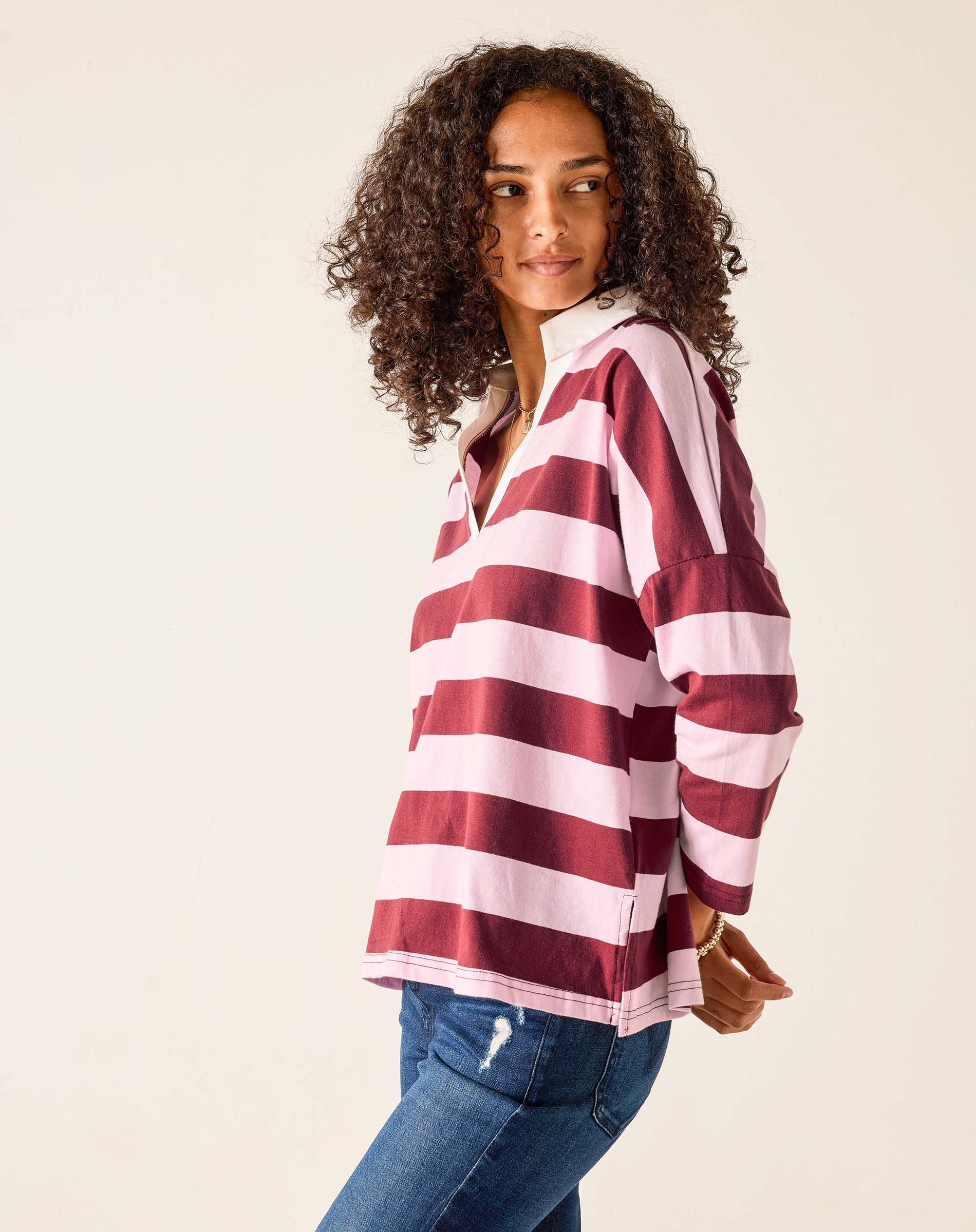 Woman wearing a maroon and white striped shirt with blue jeans on a beige background