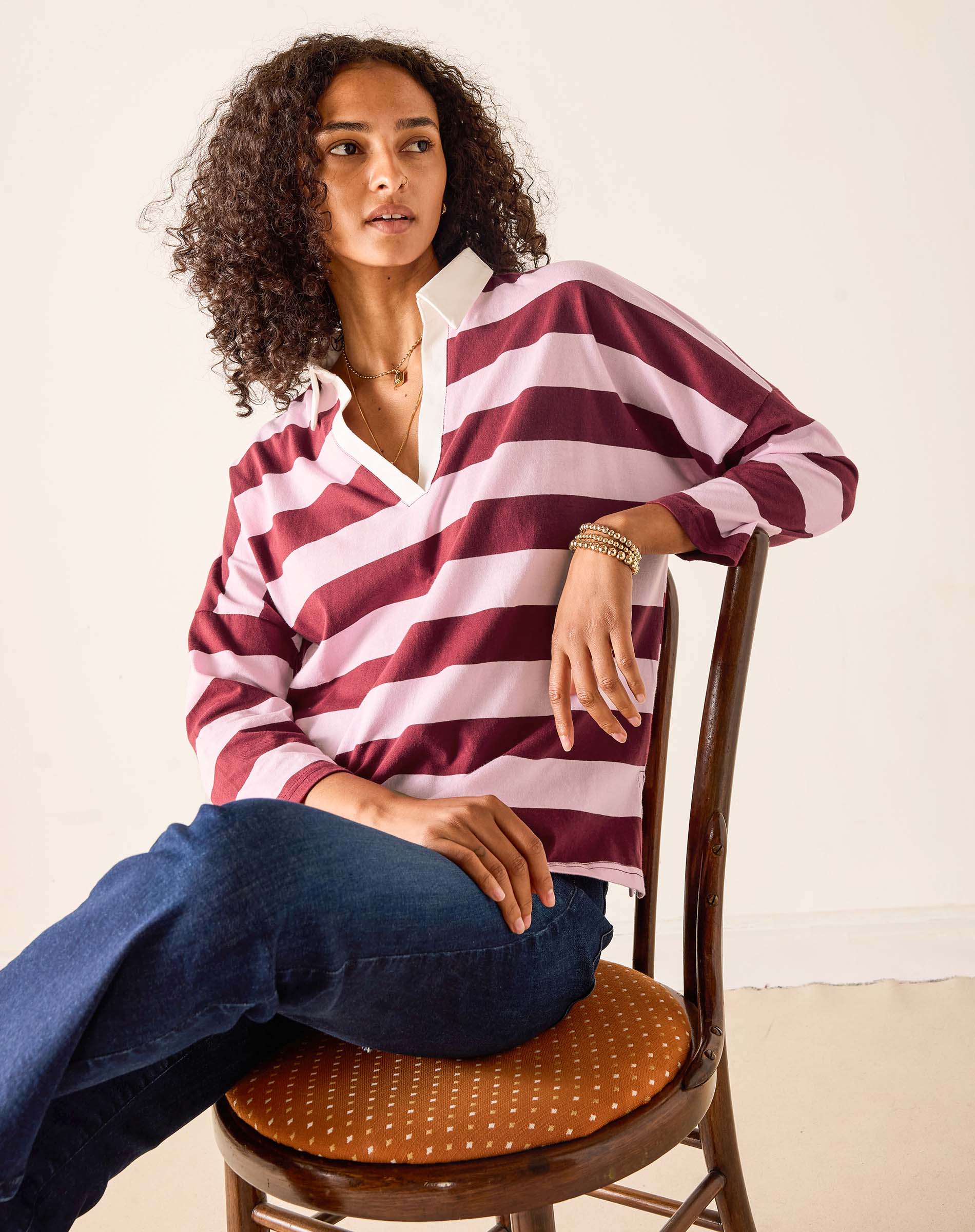 Woman wearing a red and white striped shirt sitting on a wooden chair.