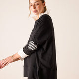 Black top featuring a white ruffled collar and a gingham print appliqué on the sleeve.