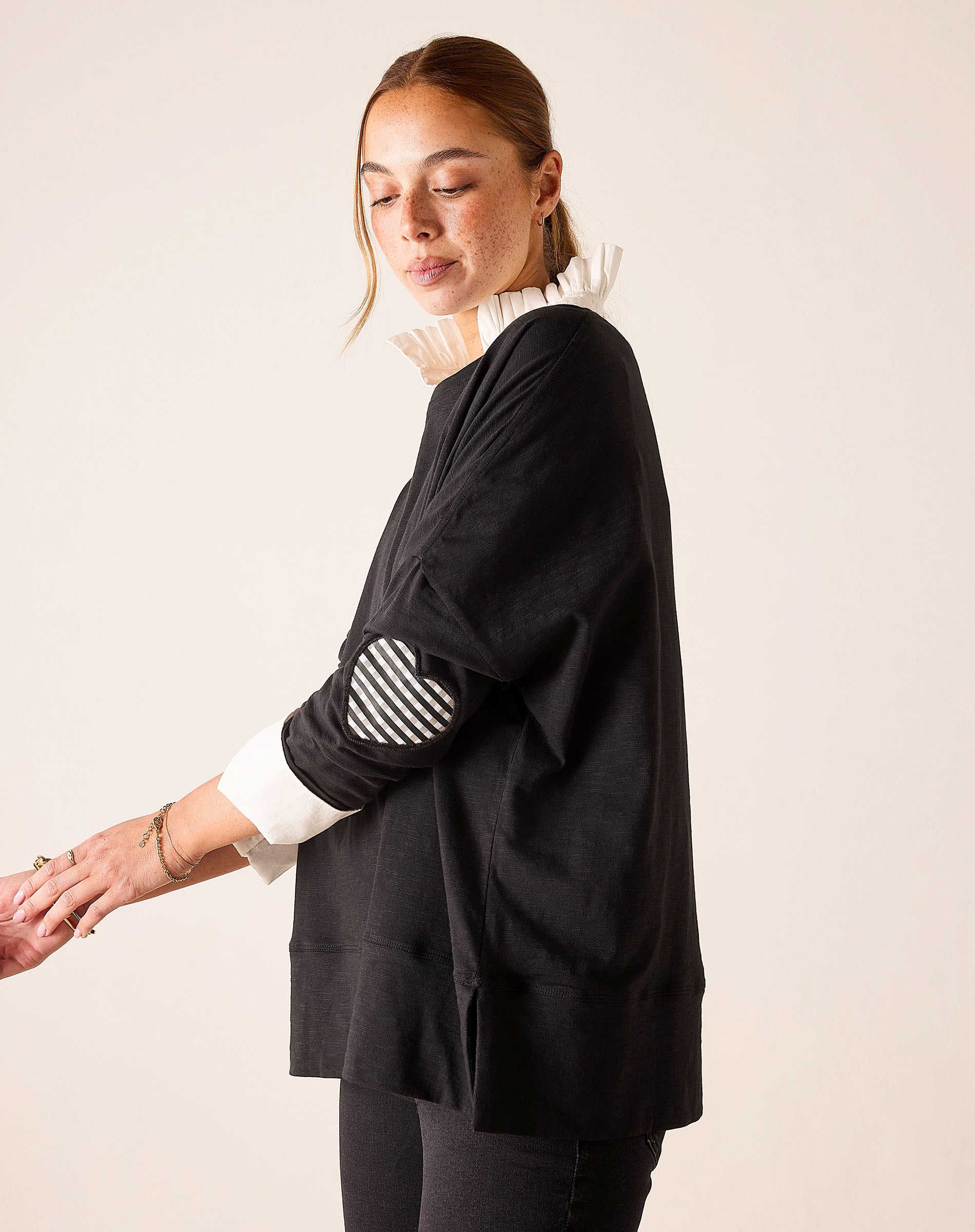 Black top featuring a white ruffled collar and a gingham print appliqué on the sleeve.