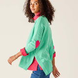 Woman wearing a green jacket with pink accents on a plain background