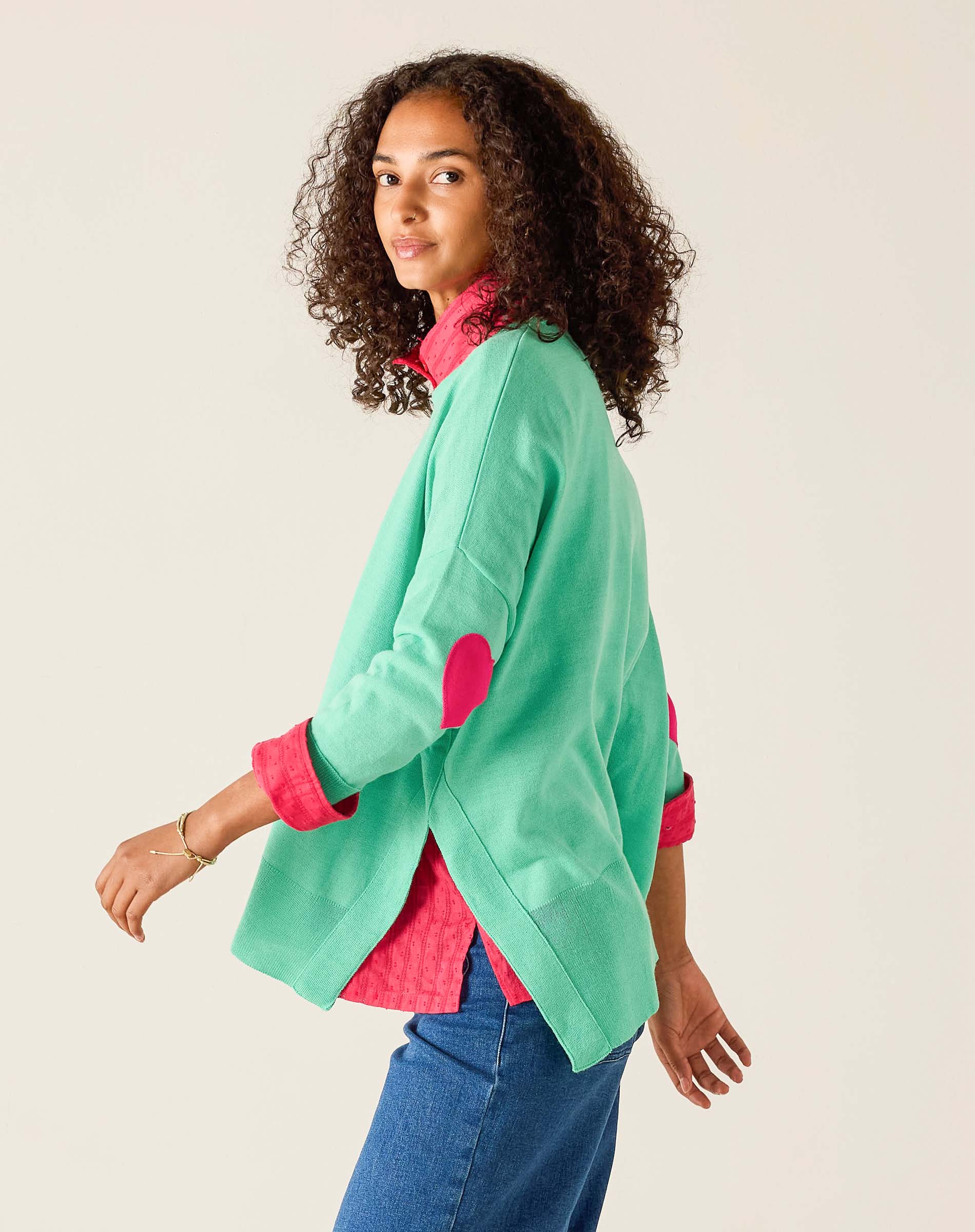Woman wearing a green jacket with pink accents on a plain background