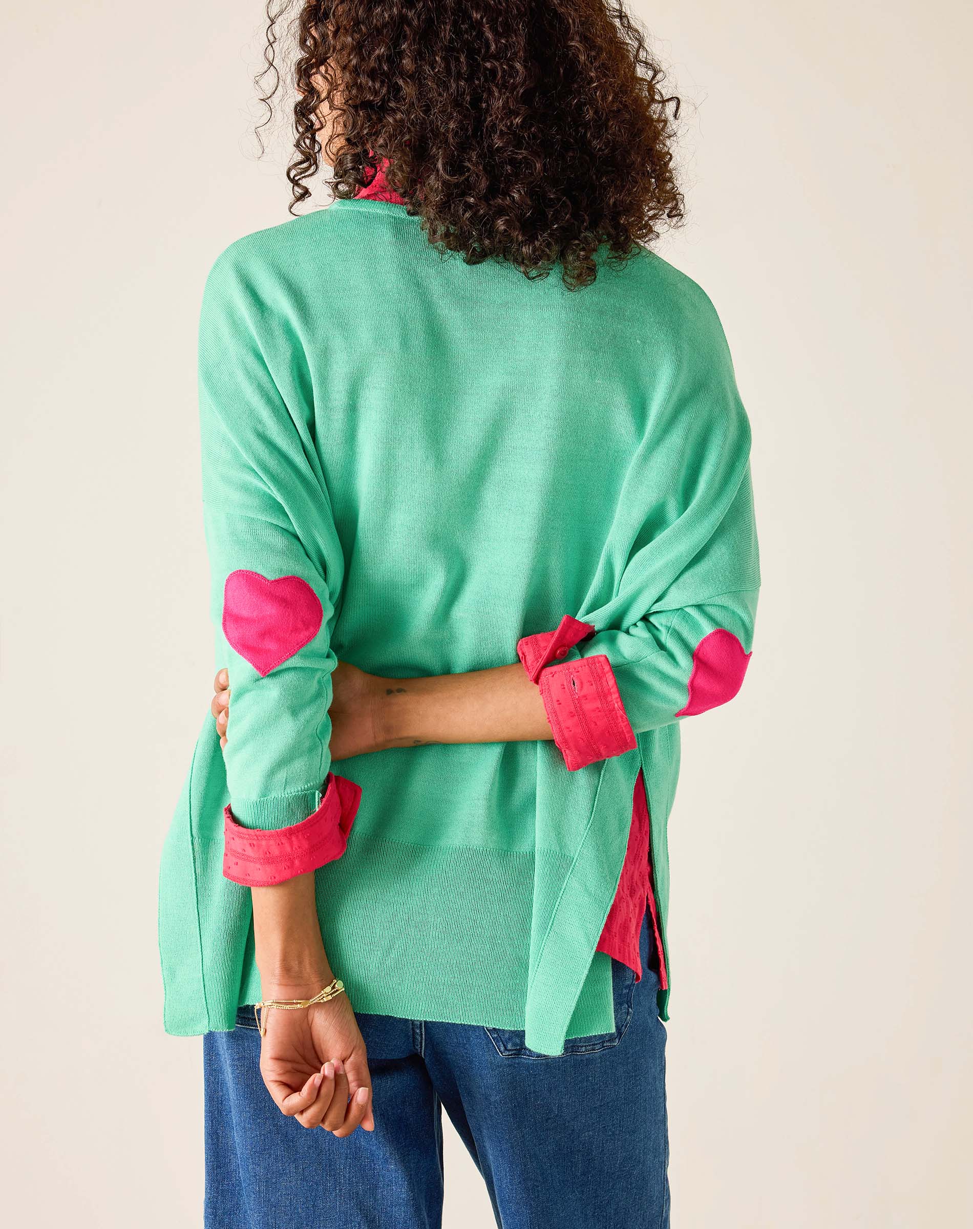 Person wearing a green top with pink cuffs and hem on a plain background