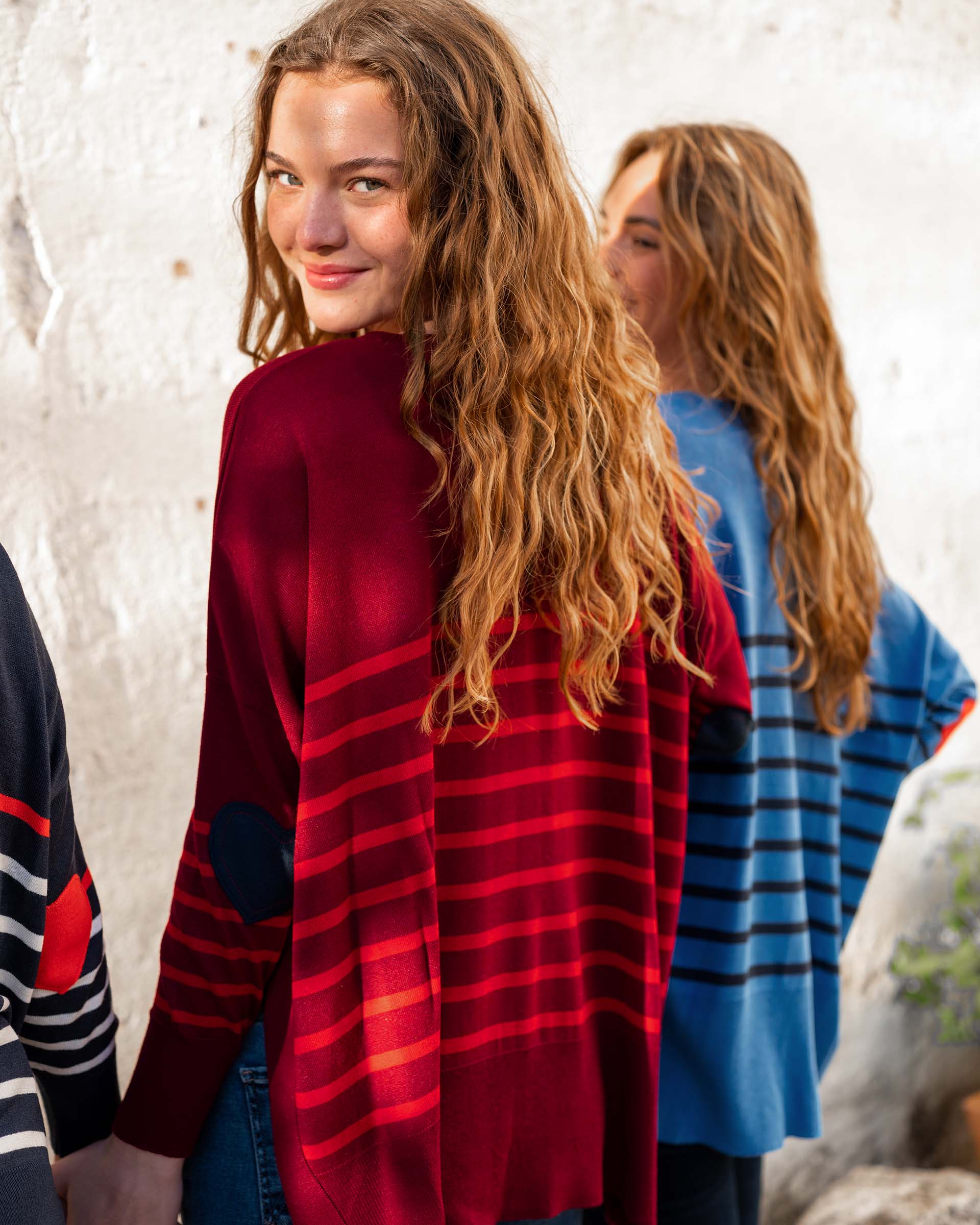 female wearing maroon and red striped sweater in front of white wall with friends