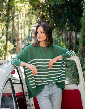 female wearing green sweater with white stripes standing near a white car door outside in Italy