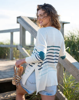 female wearing white, blue, green striped sweater with heart elbow patch walking up beach stairs