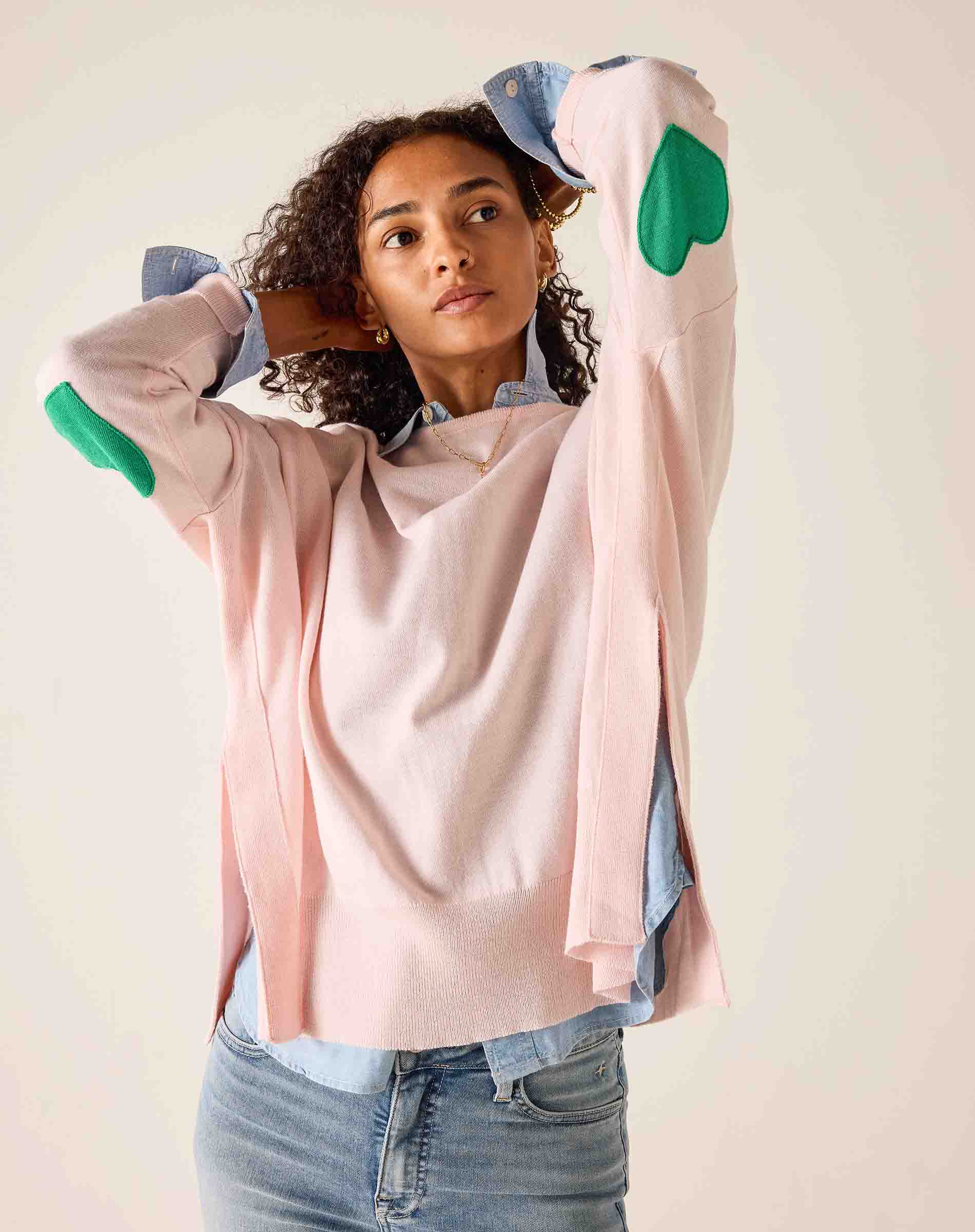 Woman wearing a light pink sweater with colorful elbow patches on a plain background