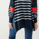 female wearing navy sweater with white stripes & red heart elbow patch backward on white background