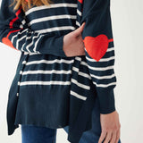 female wearing navy sweater with white stripes & red heart elbow patch backward on white background