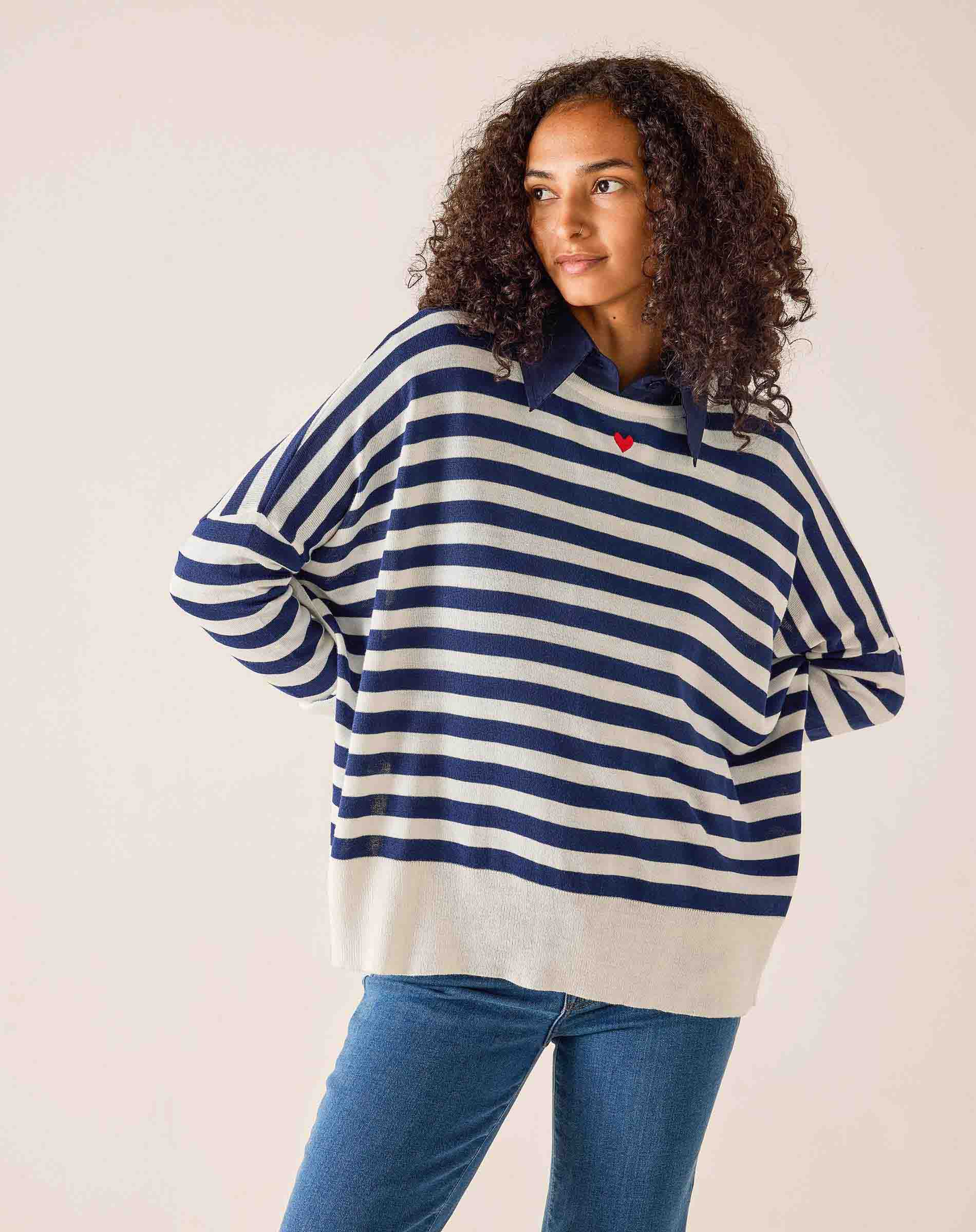 Person wearing a blue and white striped sweater with a red heart emblem on a plain background