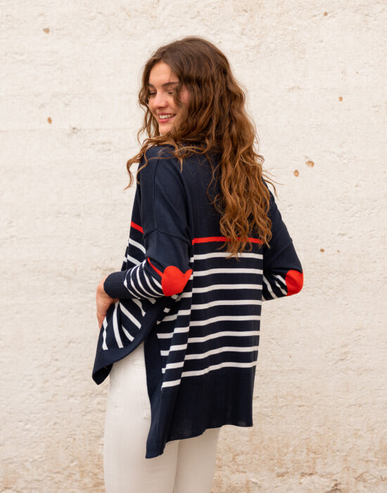 female wearing navy sweater with white stripes & red heart elbow patch backward on white wall