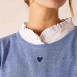 Ocean blue knit sweater with a small heart embroidered on the front and layered over a white ruffled shirt.