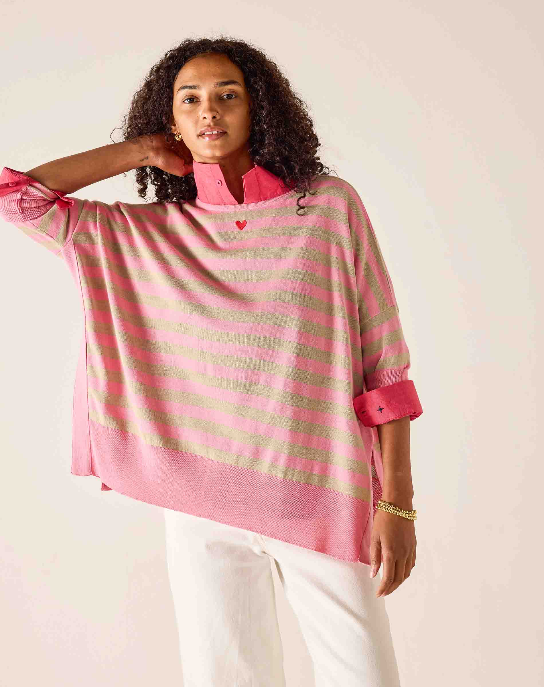Woman wearing a pink and green striped shirt with a heart design on a plain background