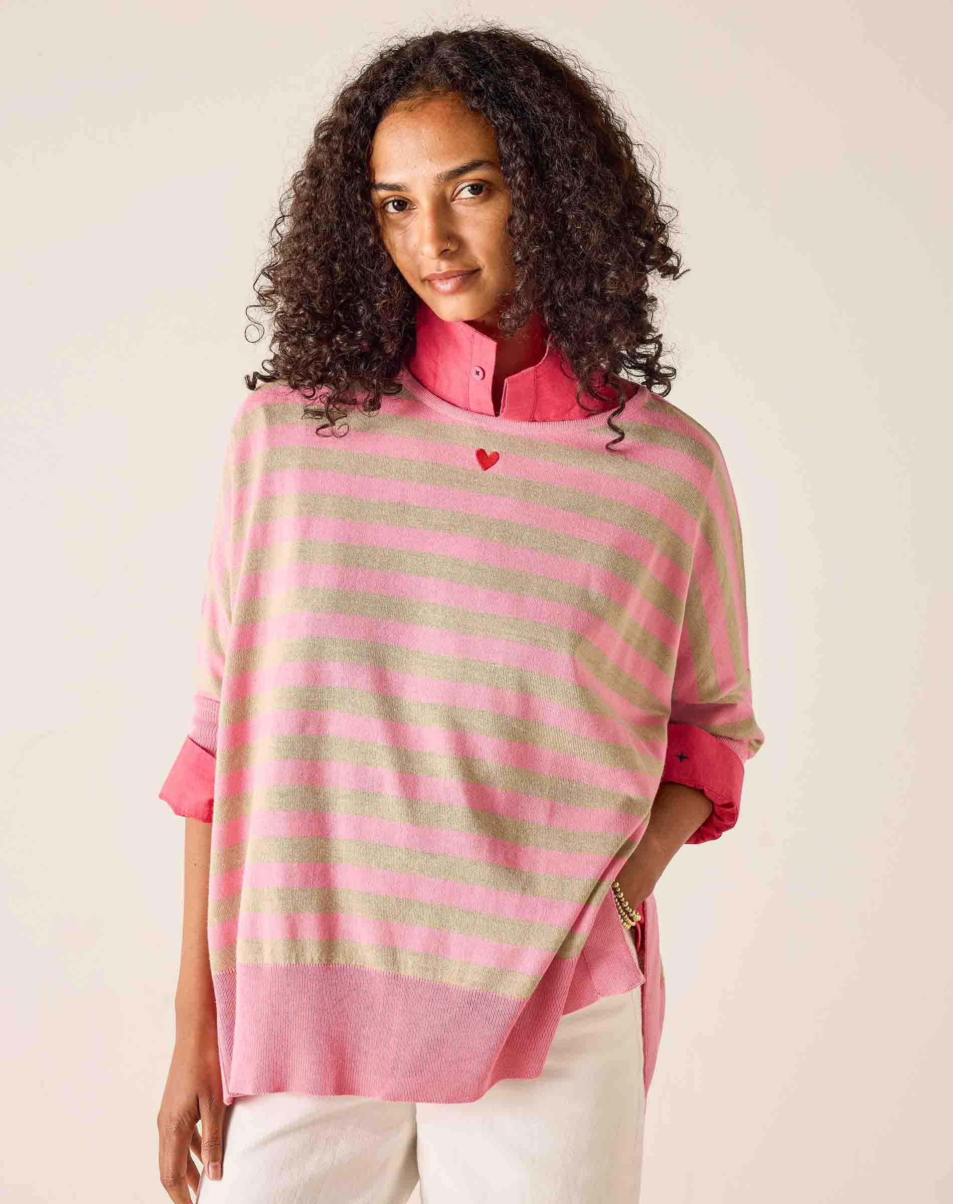 Woman wearing a pink and beige striped poncho over a pink shirt on a plain background