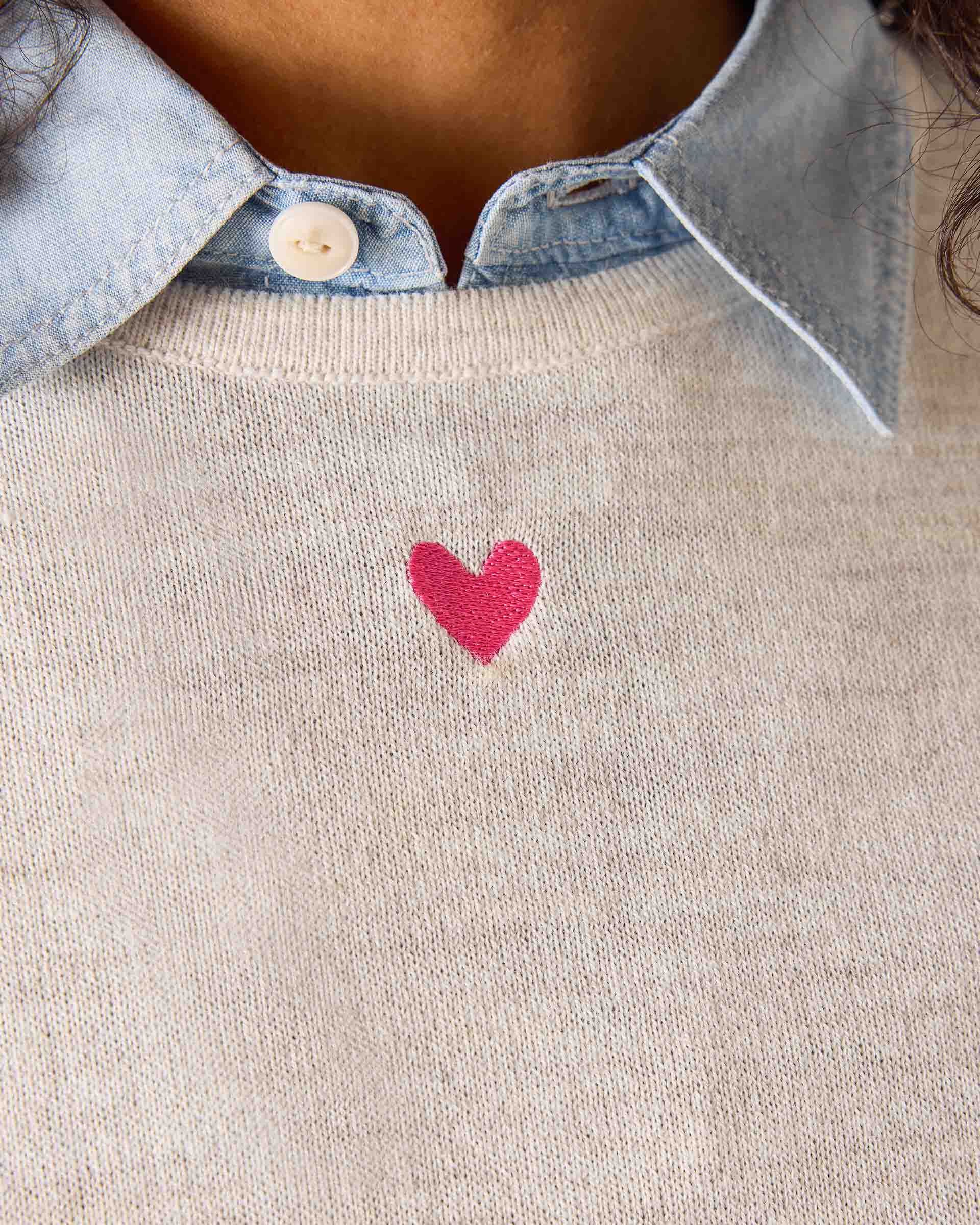 Sea salt pink knit sweater with a small embroidered heart and layered over a light blue button-down shirt.