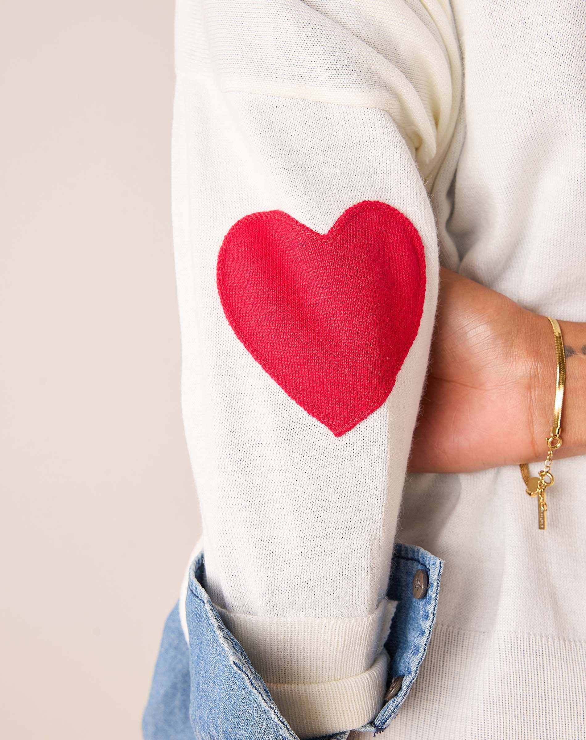 White knit sweater featuring a large red heart graphic on the sleeve.