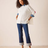 White oversized knit sweater with red accent and layered blue striped shirt, styled with cuffed denim jeans and red loafers.