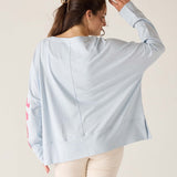 Woman wearing a light blue oversized shirt with floral sleeves on a beige background