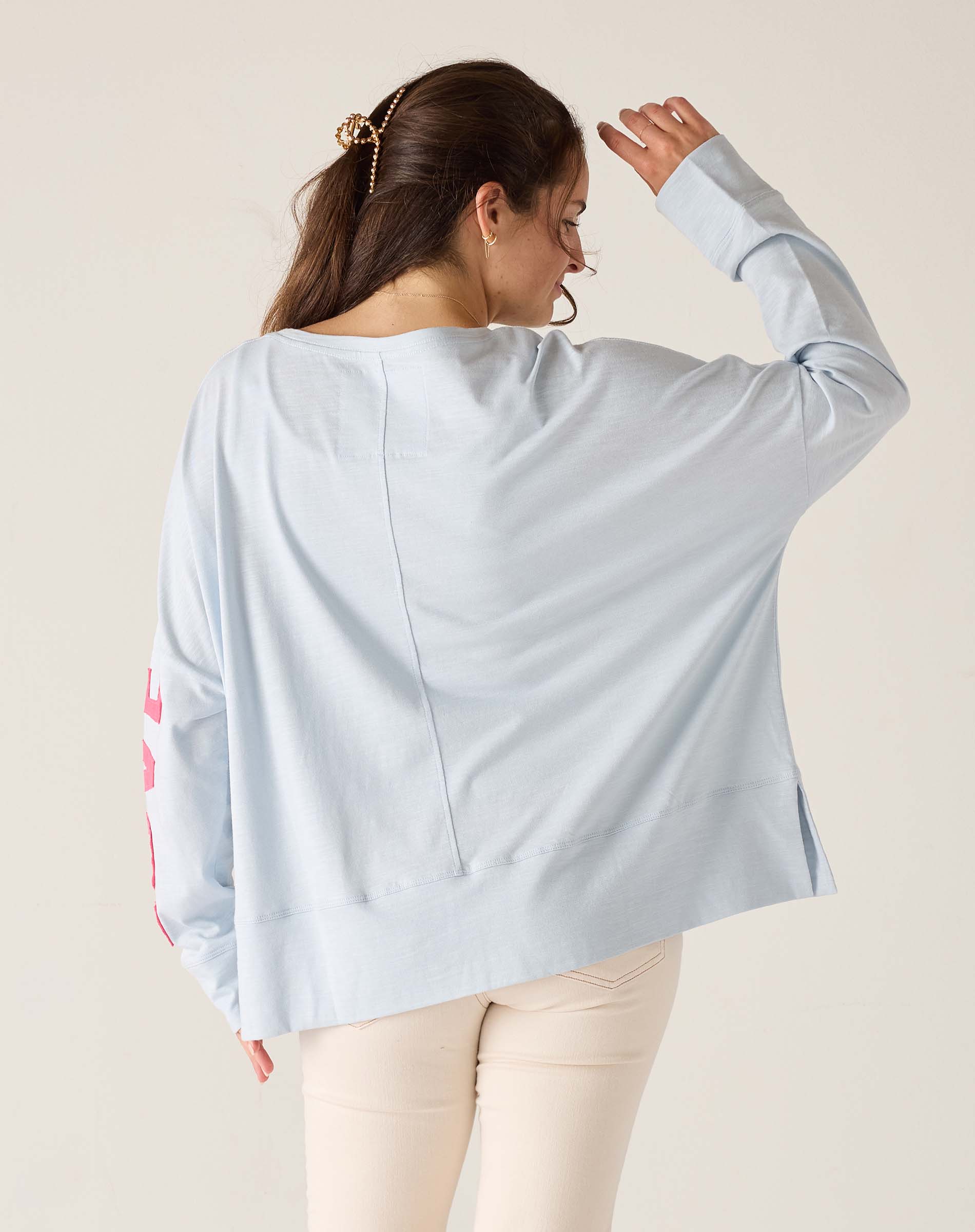 Woman wearing a light blue oversized shirt with floral sleeves on a beige background