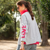 Woman wearing a gray sweatshirt with 'LOVE' printed on it in a park.