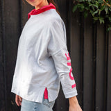 Woman wearing a gray sweatshirt with red accents and sunglasses, standing against a dark background.