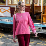Woman in pink long-sleeve top and red pants walking past a trolley car.