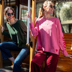 Two women on a trolley, one in a green top and blue jeans, the other in a pink sweatshirt and red pants.