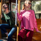 Two women on a trolley, one in a green top and blue jeans, the other in a pink sweatshirt and red pants.