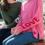 Two people sitting on a bench, one wearing a green shirt with 'LOVE' and the other in a pink sweater with 'LOVE' and heart designs.