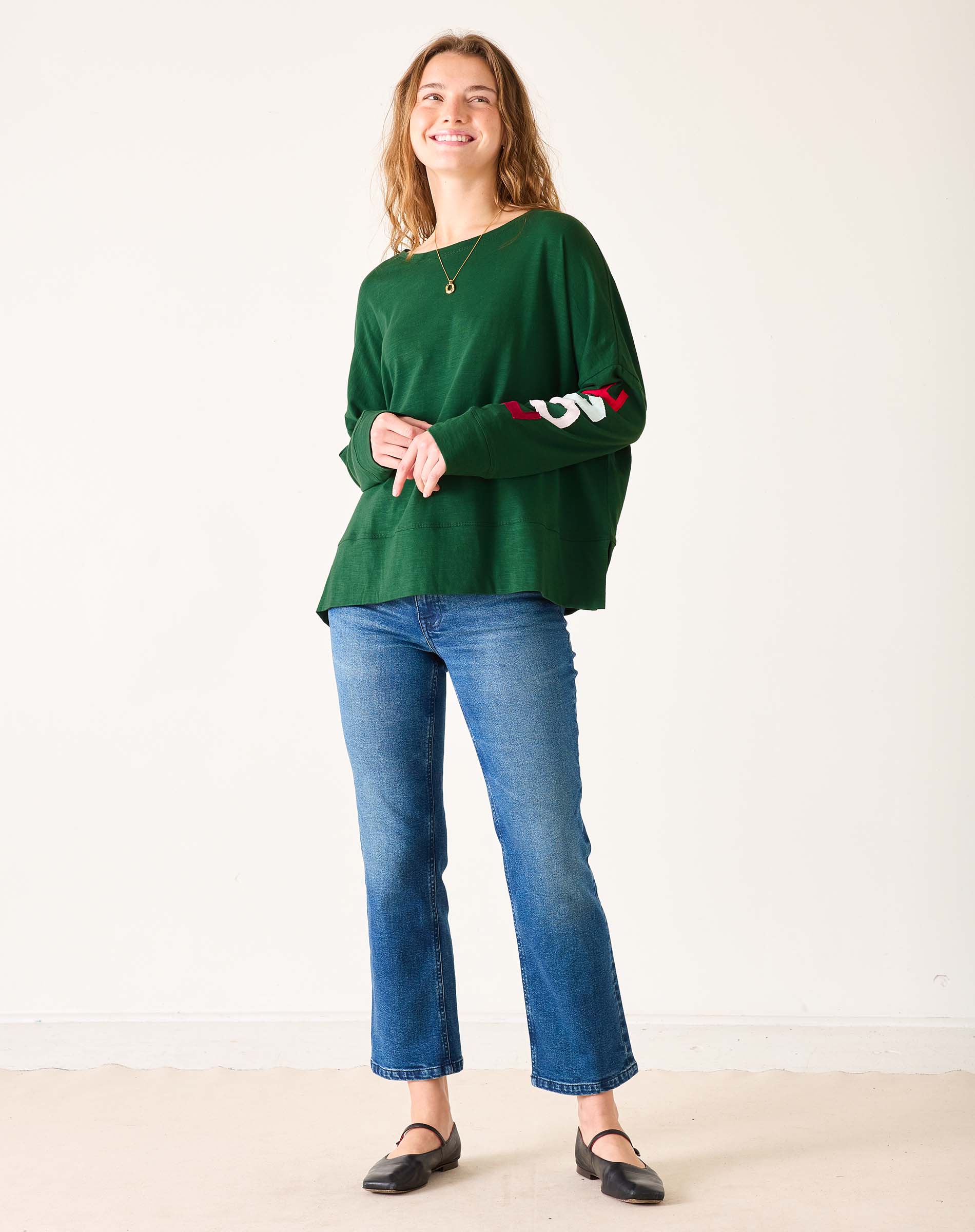 Woman wearing a green sweater with 'LOVE' text and blue jeans on a white background