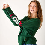 Woman wearing a green sweatshirt with 'LOVE' printed on the sleeve against a white background