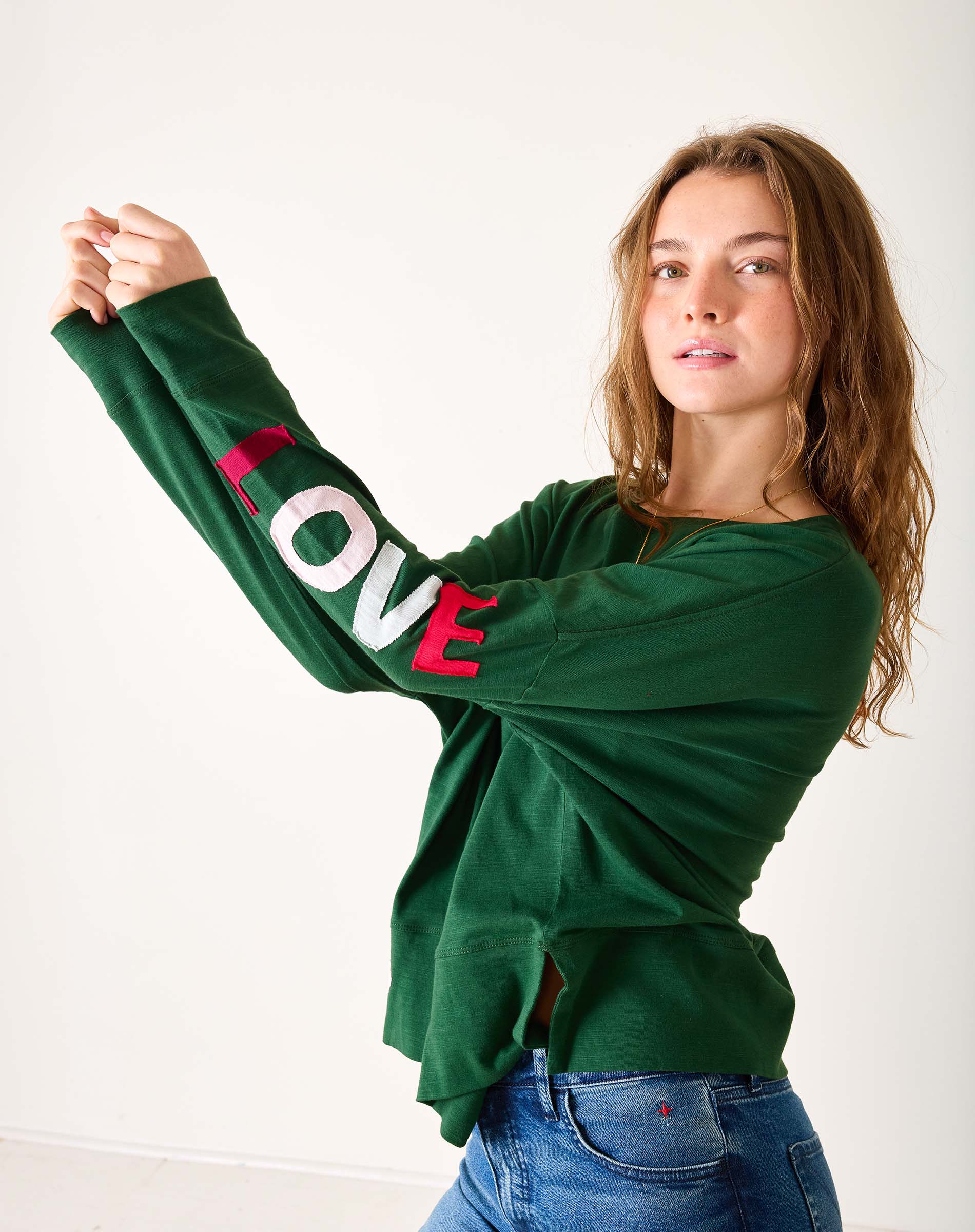 Woman wearing a green sweatshirt with 'LOVE' printed on the sleeve against a white background