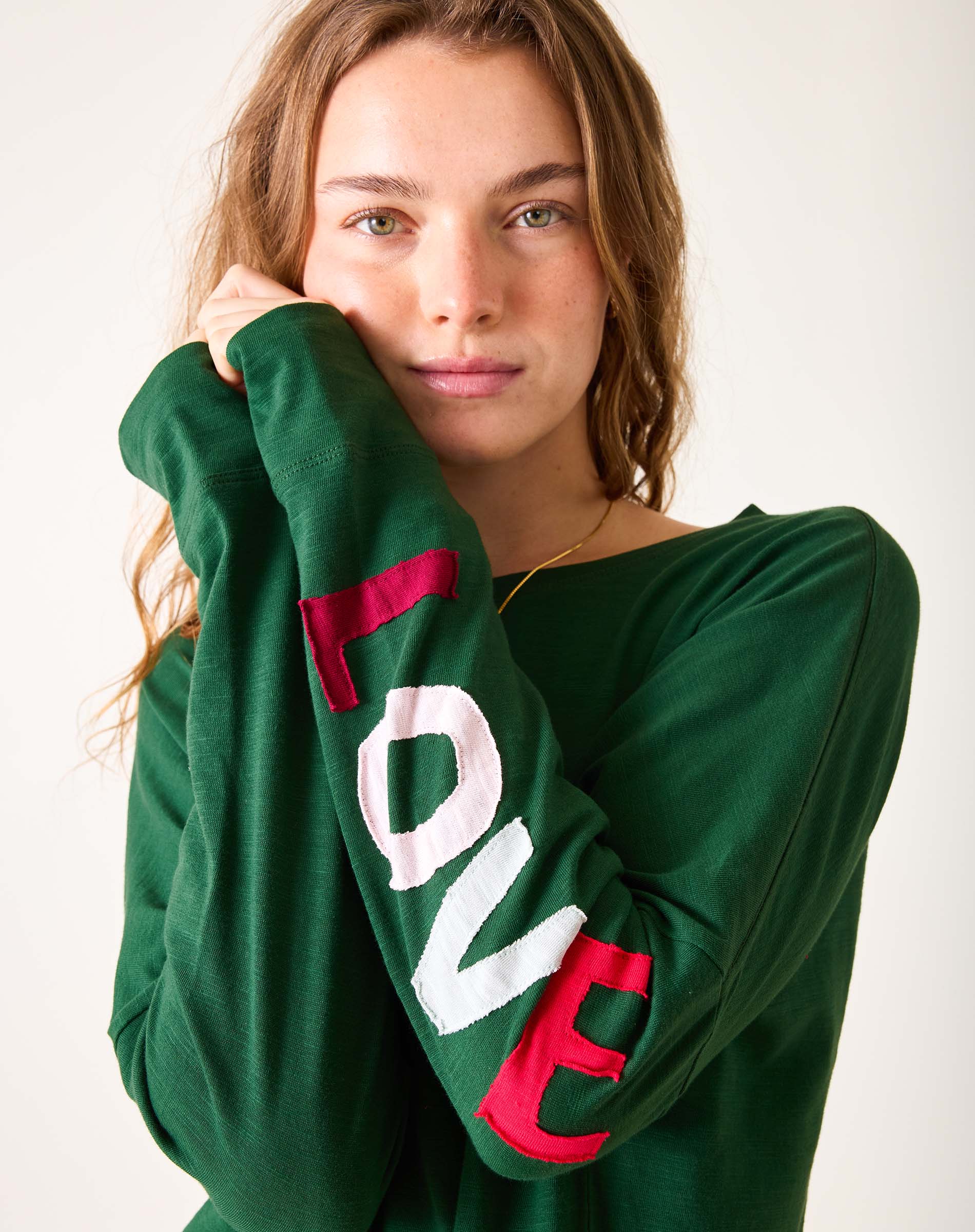 Person wearing a green sweatshirt with 'LOVE' printed on the sleeves against a white background