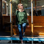 Woman sitting on a vintage trolley wearing a green sweater and blue jeans.