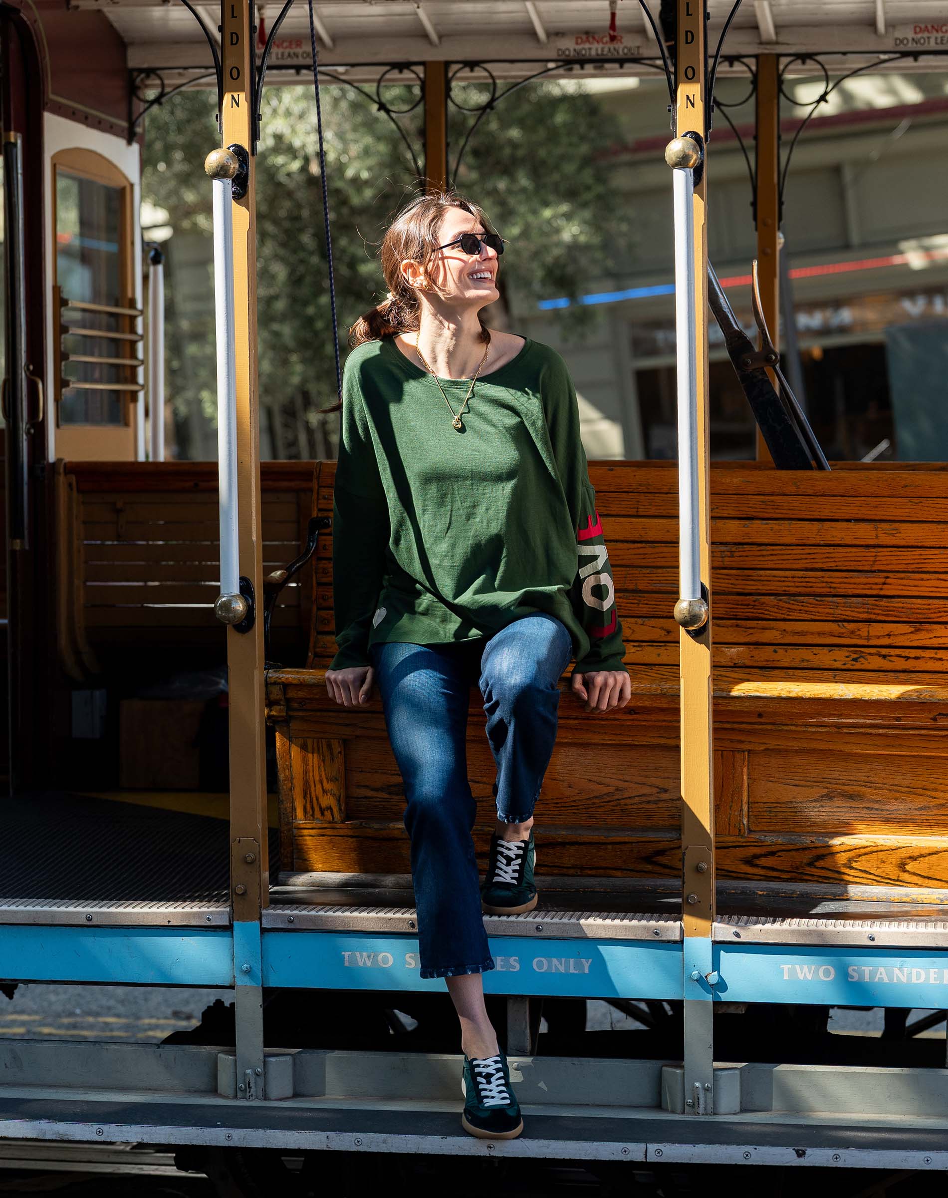 Woman sitting on a vintage trolley wearing a green sweater and blue jeans.